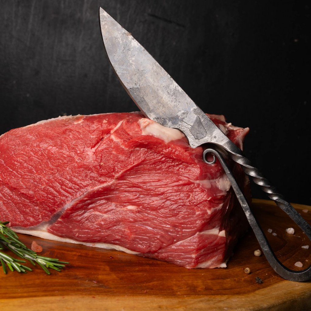 Raw meat with a knife on a wooden board against a dark background