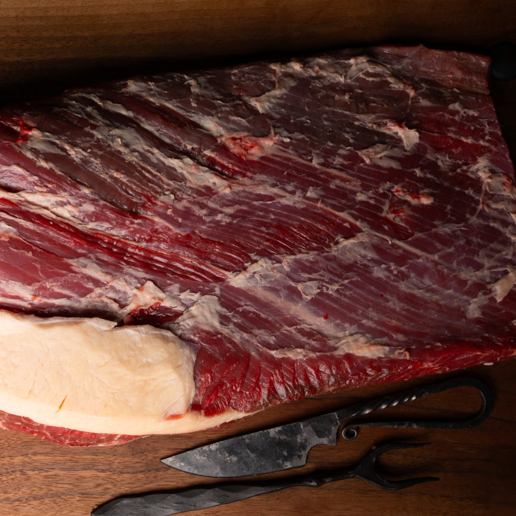 Raw meat on a wooden cutting board with a knife and scissors.