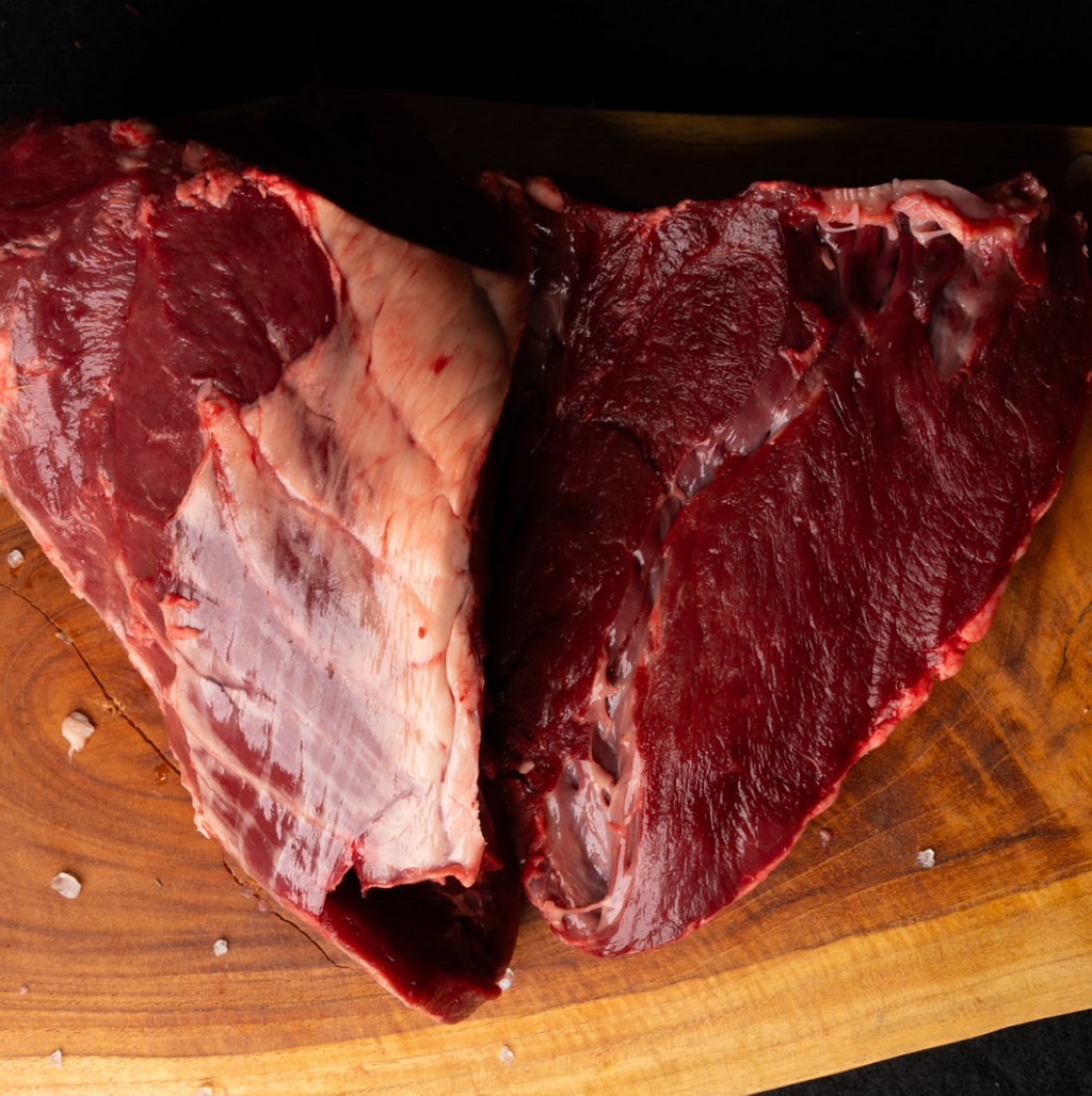Two pieces of raw beef on a wooden cutting board