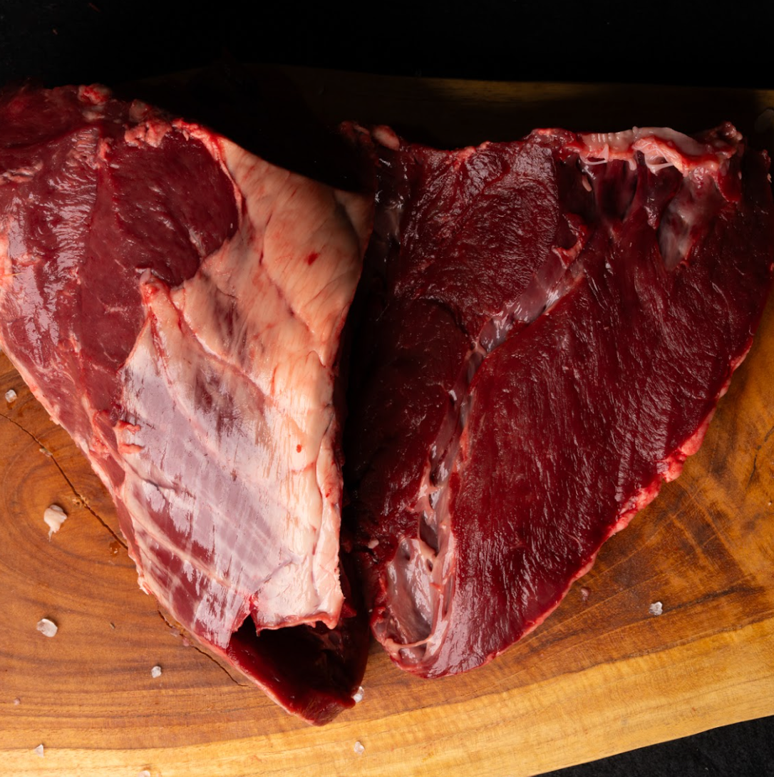 Two pieces of raw beef on a wooden cutting board