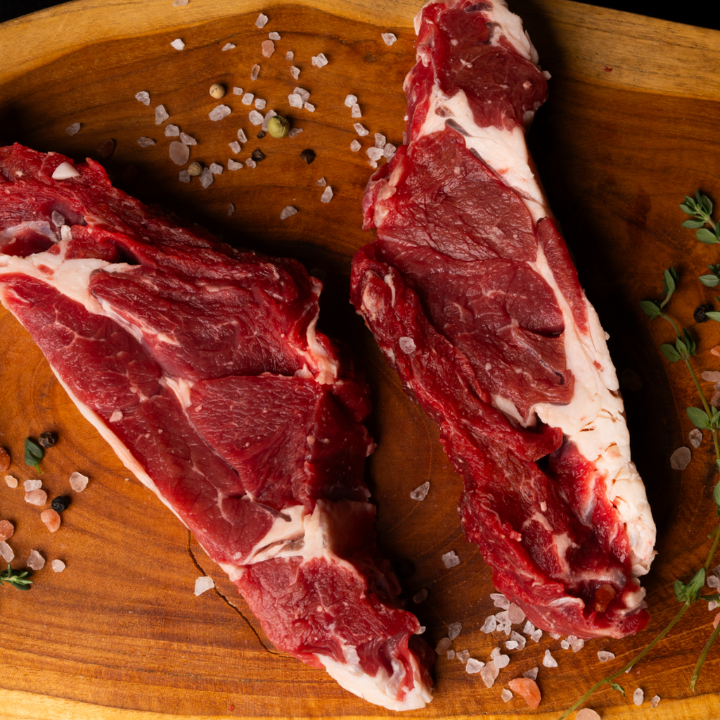 Two pieces of raw meat on a wooden cutting board with salt and herbs.