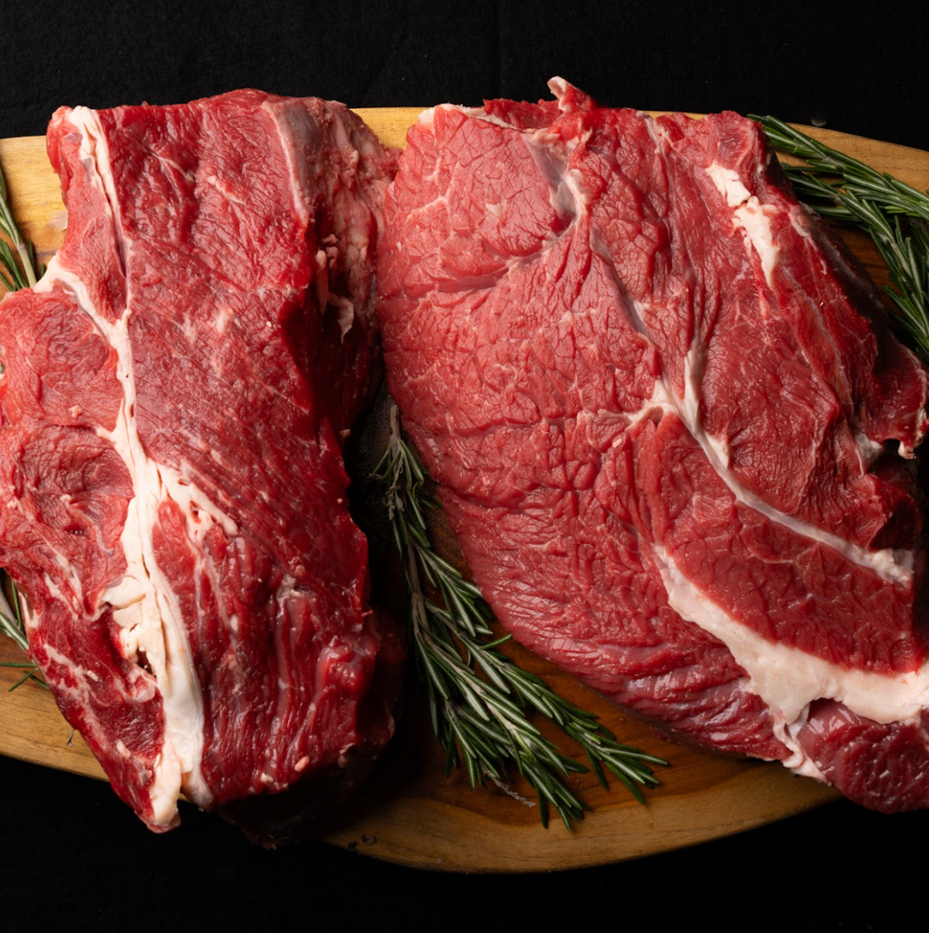 Two large pieces of raw beef on a wooden cutting board with rosemary sprigs.