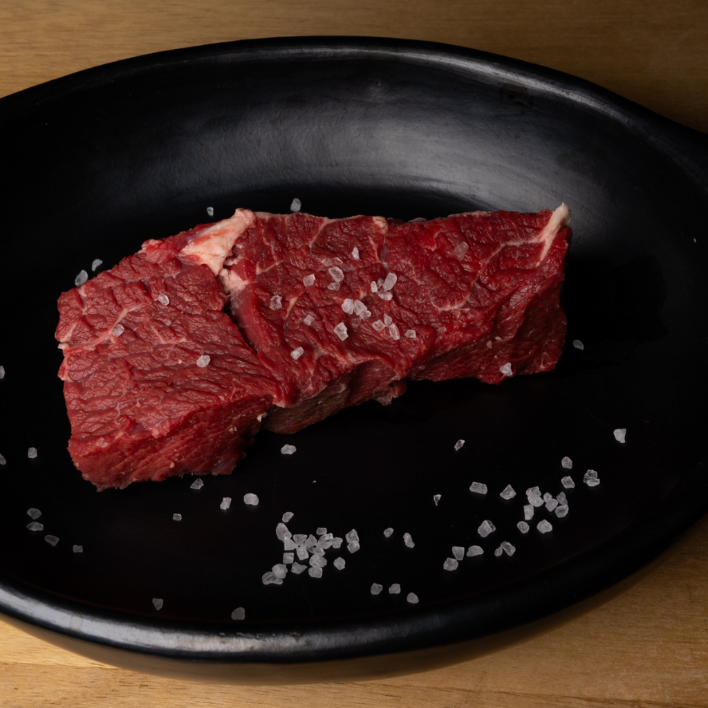 Raw beef on a black plate with salt crystals on a wooden surface