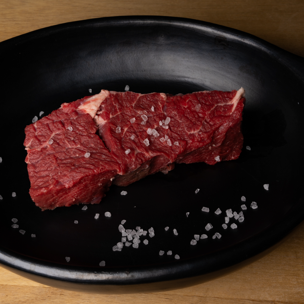 Raw beef on a black plate with salt crystals on a wooden surface