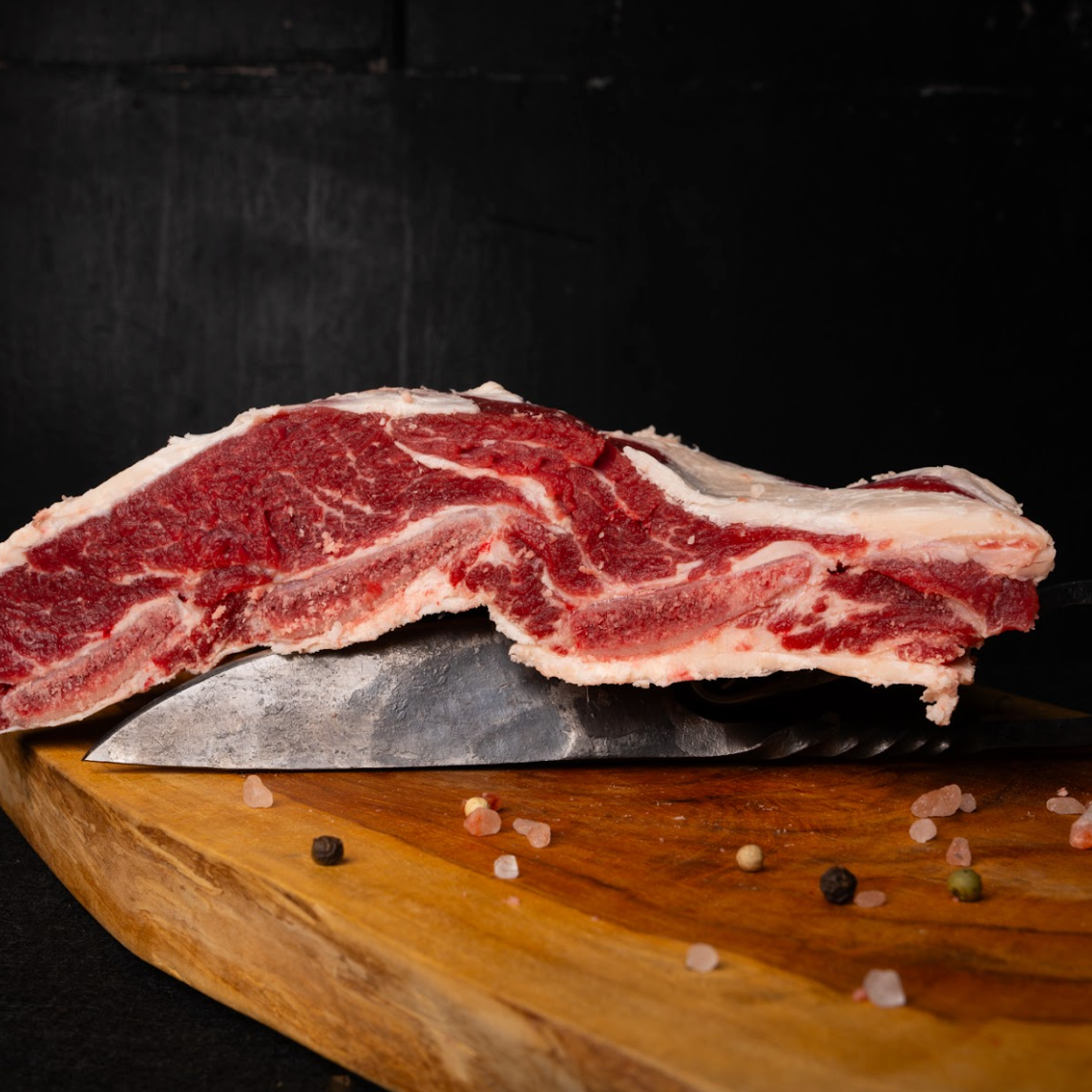 Raw steak on a wooden cutting board with a knife, black background