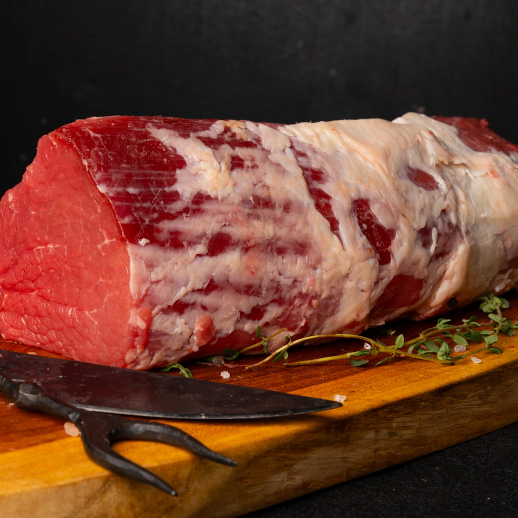 Raw meat roll on a wooden board with a knife and thyme sprigs, dark background