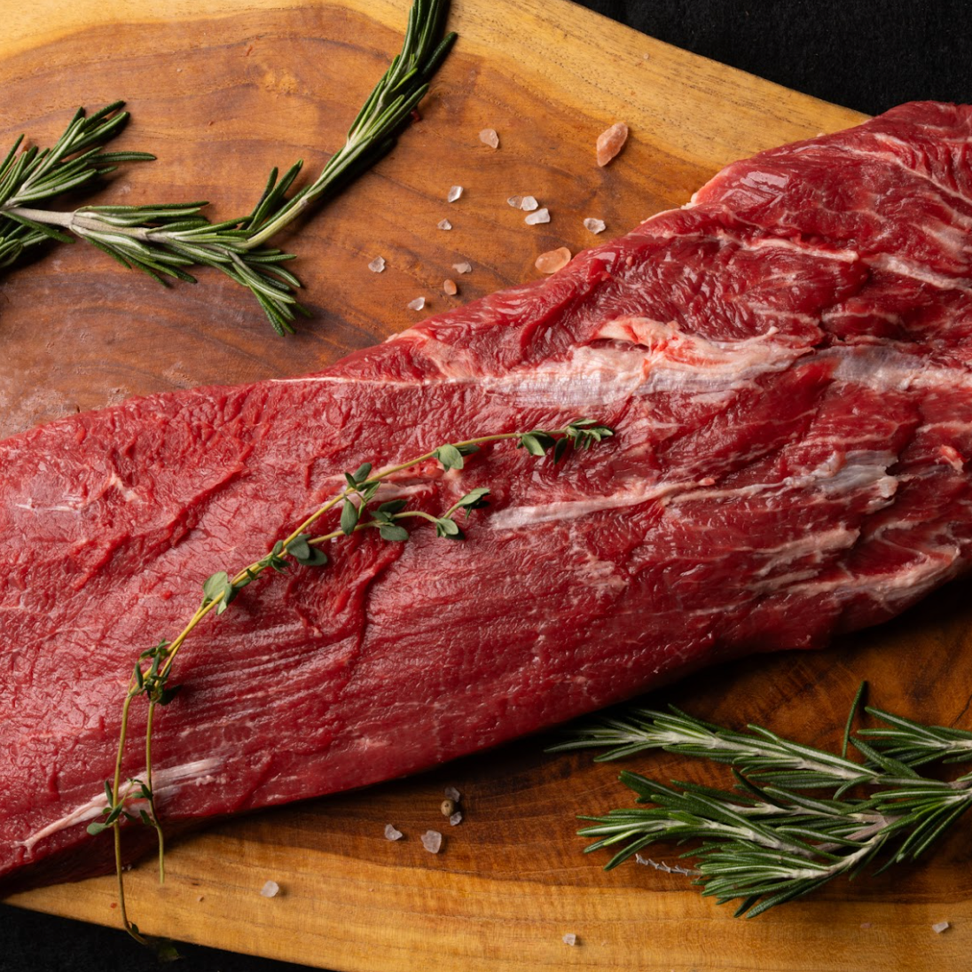 Raw beef on a wooden cutting board with herbs