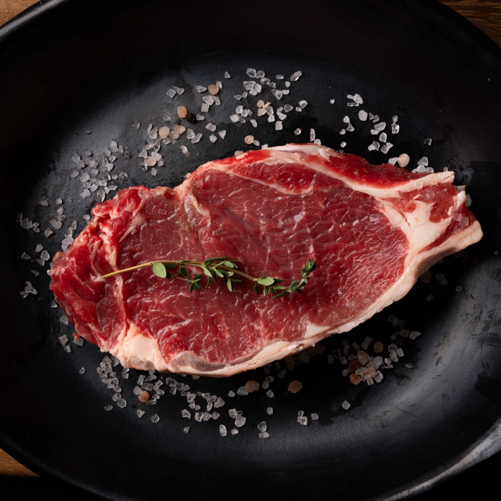 Raw steak on a black plate with salt and thyme