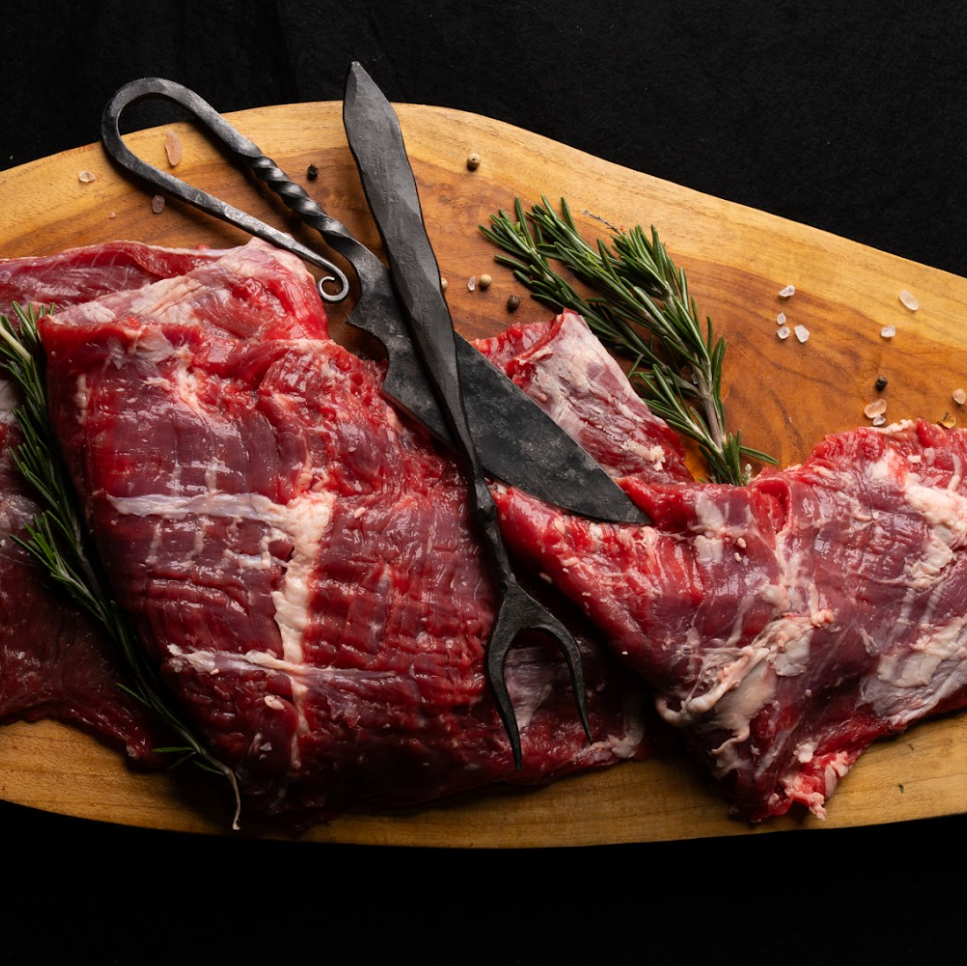 Raw meat on a wooden cutting board with rosemary and a knife.