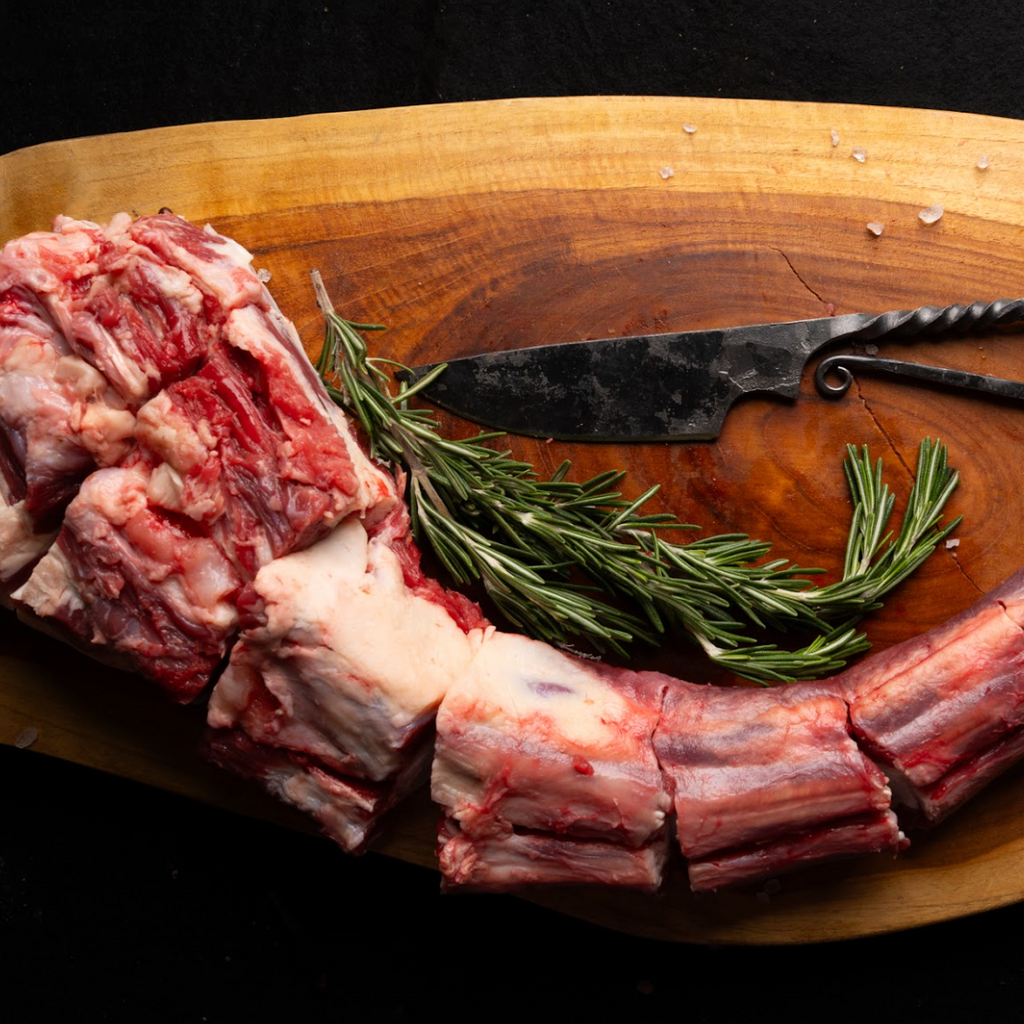 Raw meat with rosemary on a wooden cutting board with a knife.