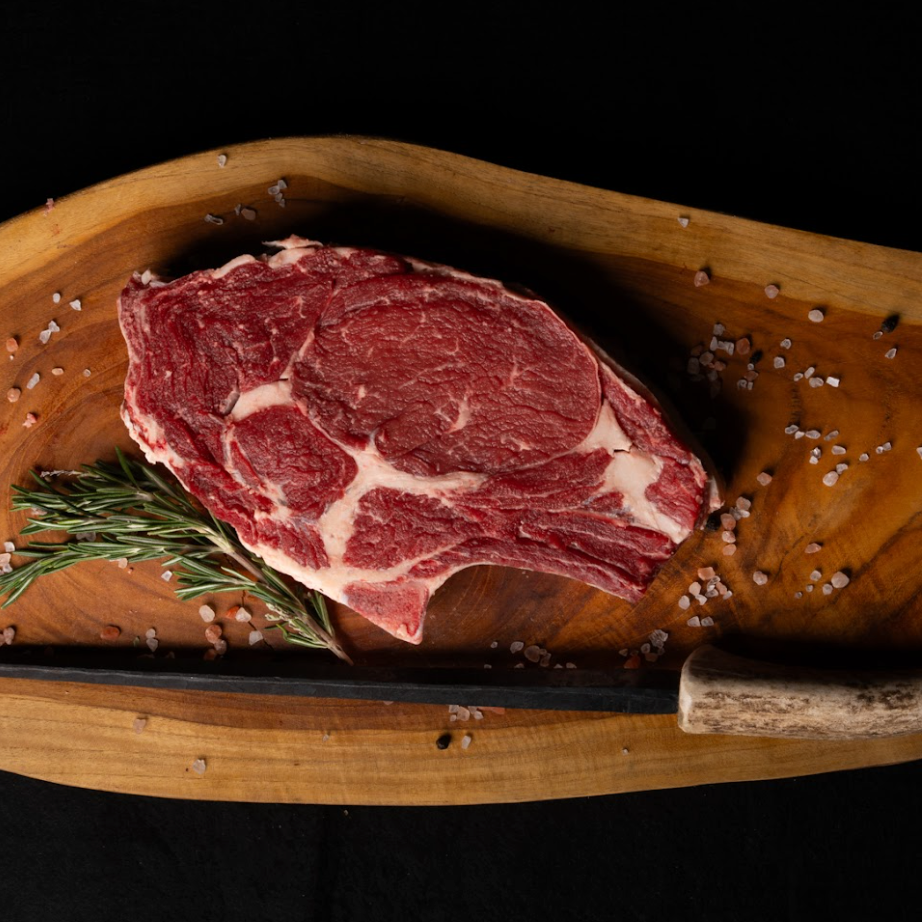 Raw steak on a wooden cutting board with rosemary and salt, against a dark background
