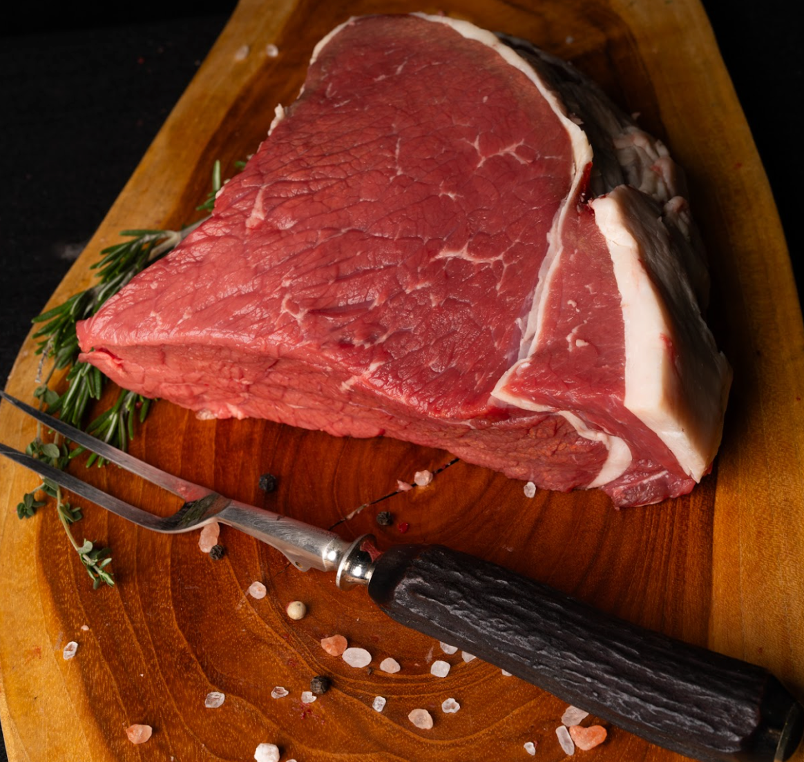 Raw steak on a wooden cutting board with a fork and herbs