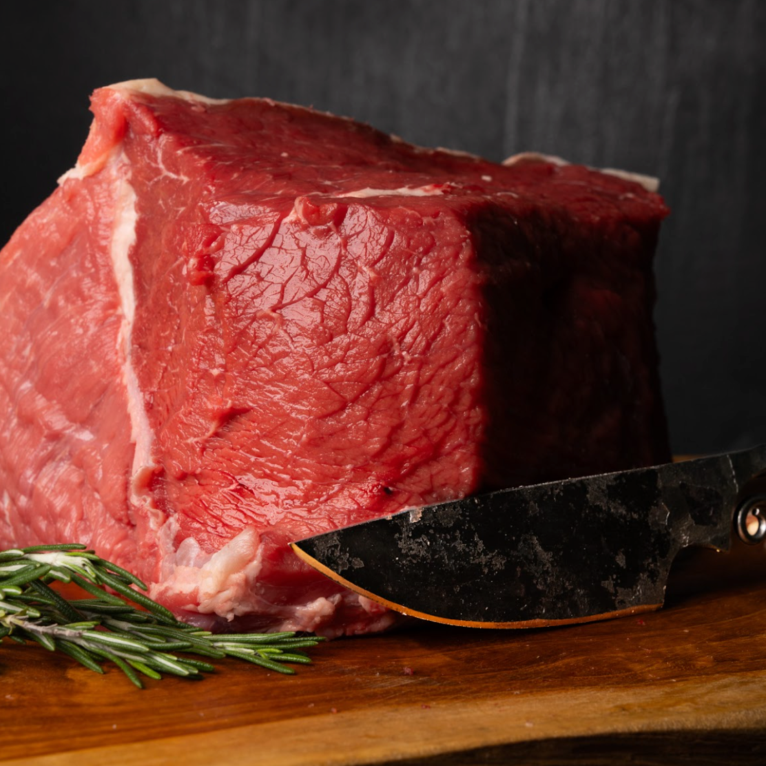 Raw steak on a wooden cutting board with a knife and rosemary sprig, against a dark background