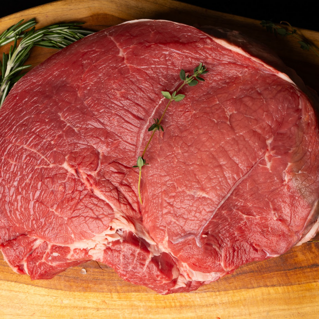 Raw beef roast on a wooden cutting board with herbs