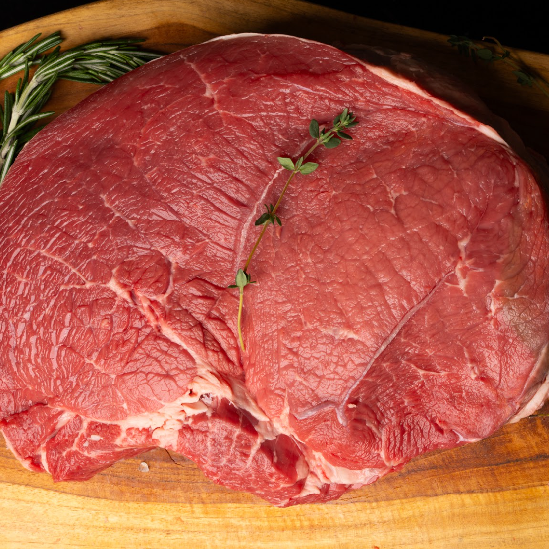 Raw beef roast on a wooden cutting board with herbs