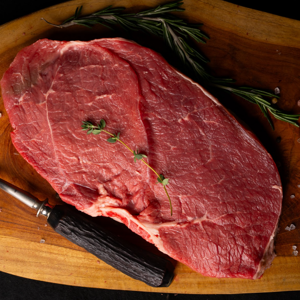 Raw steak on a wooden cutting board with herbs and a knife.