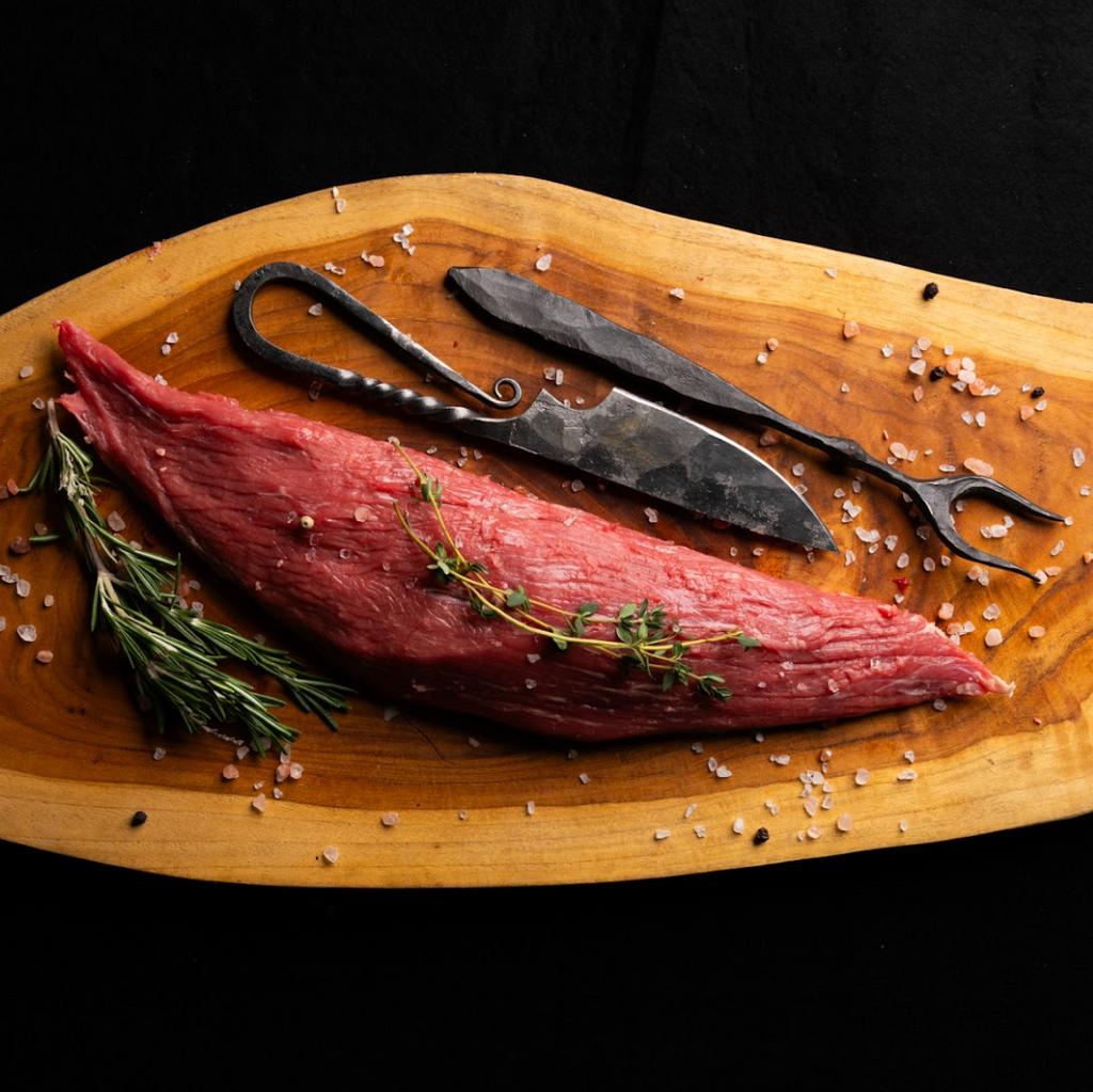 Raw beef on a wooden cutting board with rosemary, thyme, and kitchen shears.