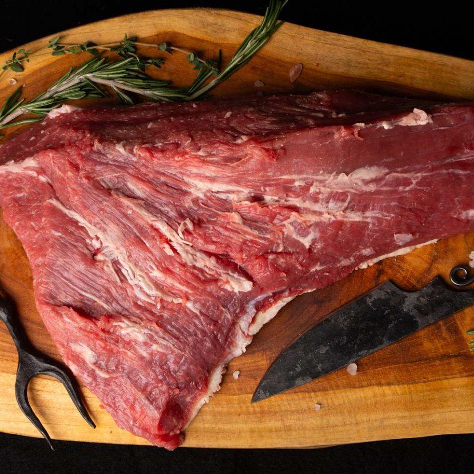 Raw beef on a wooden cutting board with a knife and rosemary.